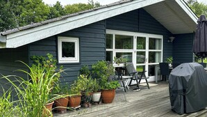 Een houten terras met plantenbakken, een overdekte barbecue en tuinmeubilair.