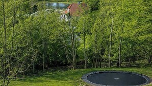 Ett grönområde med en studsmatta, en damm och en byggnad med ett rött tak i bakgrunden.