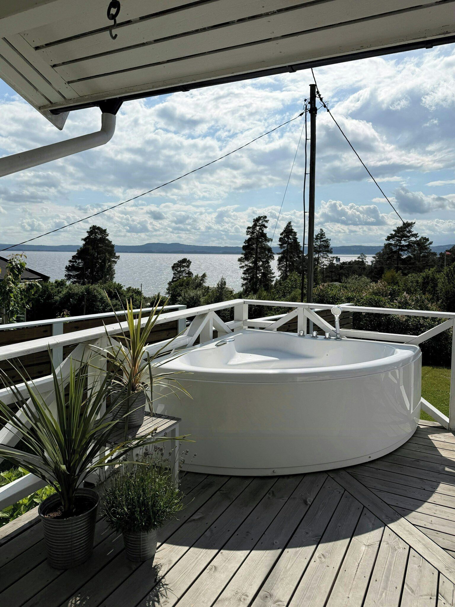 A hot tub on a wooden deck with a railing, surrounded by potted plants.