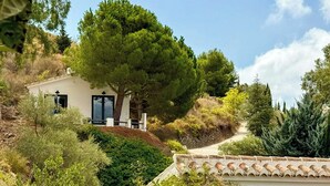 Una casa amb un arbre gran al davant, envoltada de verdura i un cel clar.