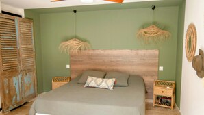 Ein Schlafzimmer mit einem Bett, einem Deckenventilator, einer grünen Wand und einer rustikalen Tür.