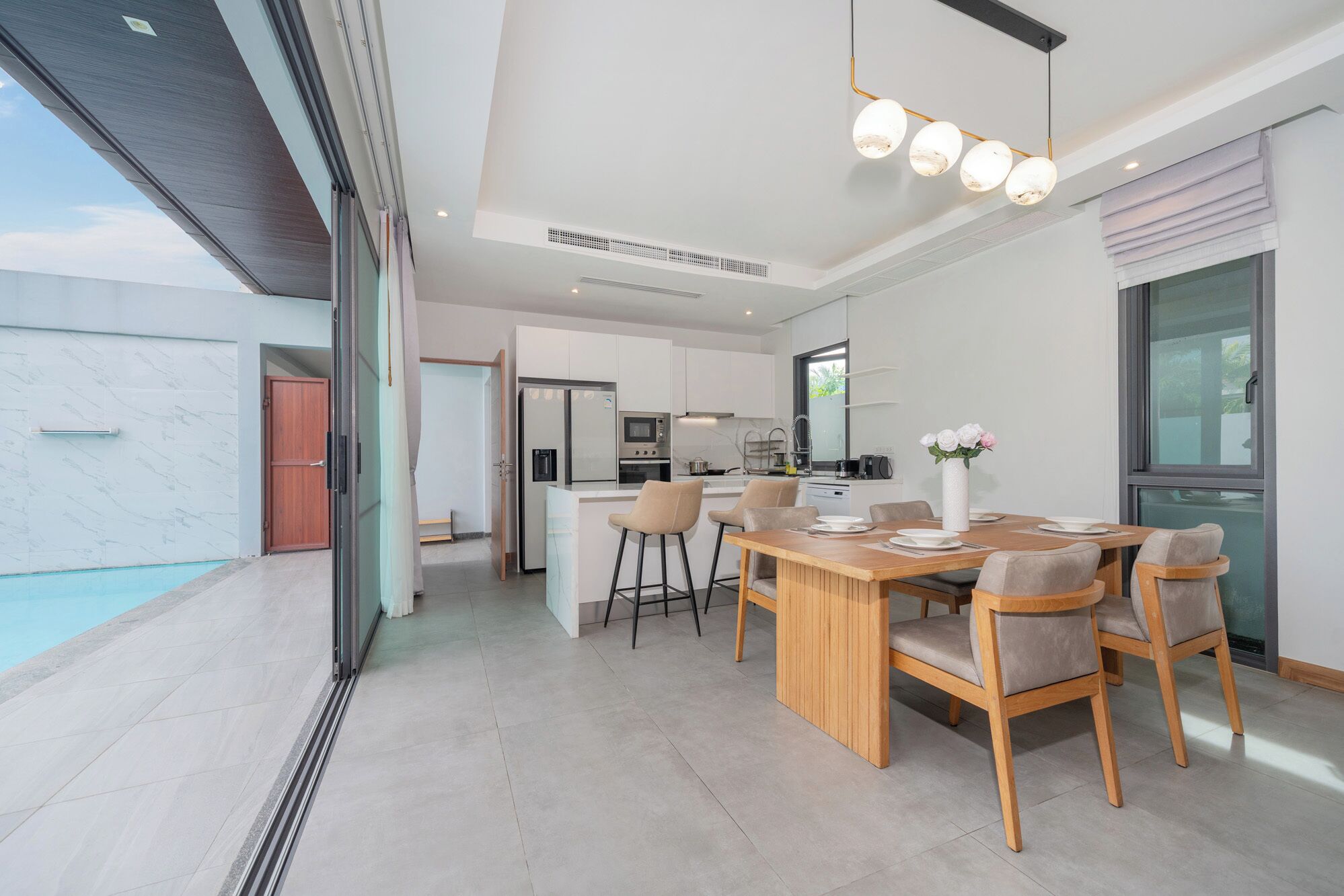 Cozinha moderna com ilha central, área de jantar com mesa e cadeiras de madeira, e uma janela grande com vista.