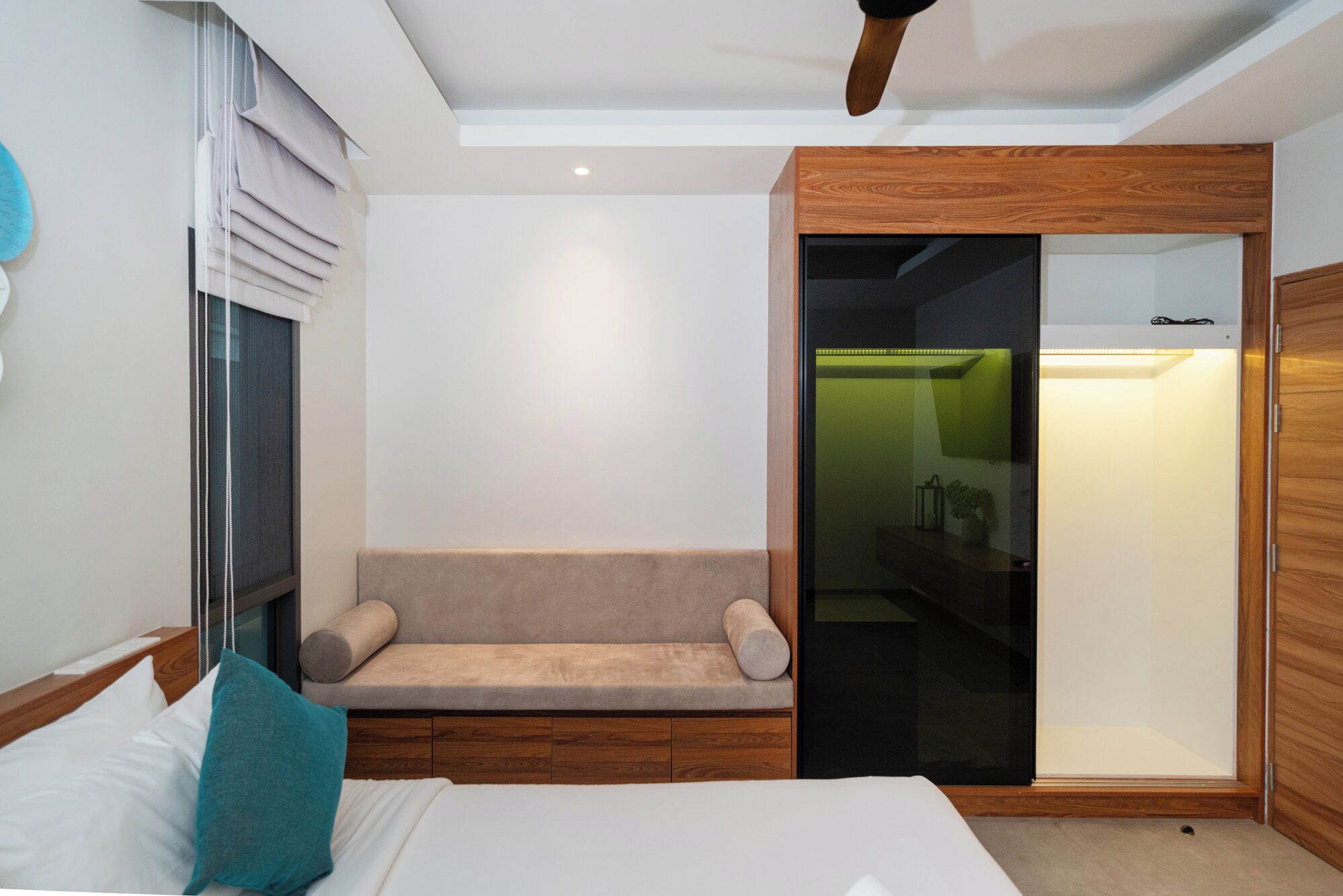 A modern hotel room with a bed, a bench, a wardrobe, and a sliding door closet.