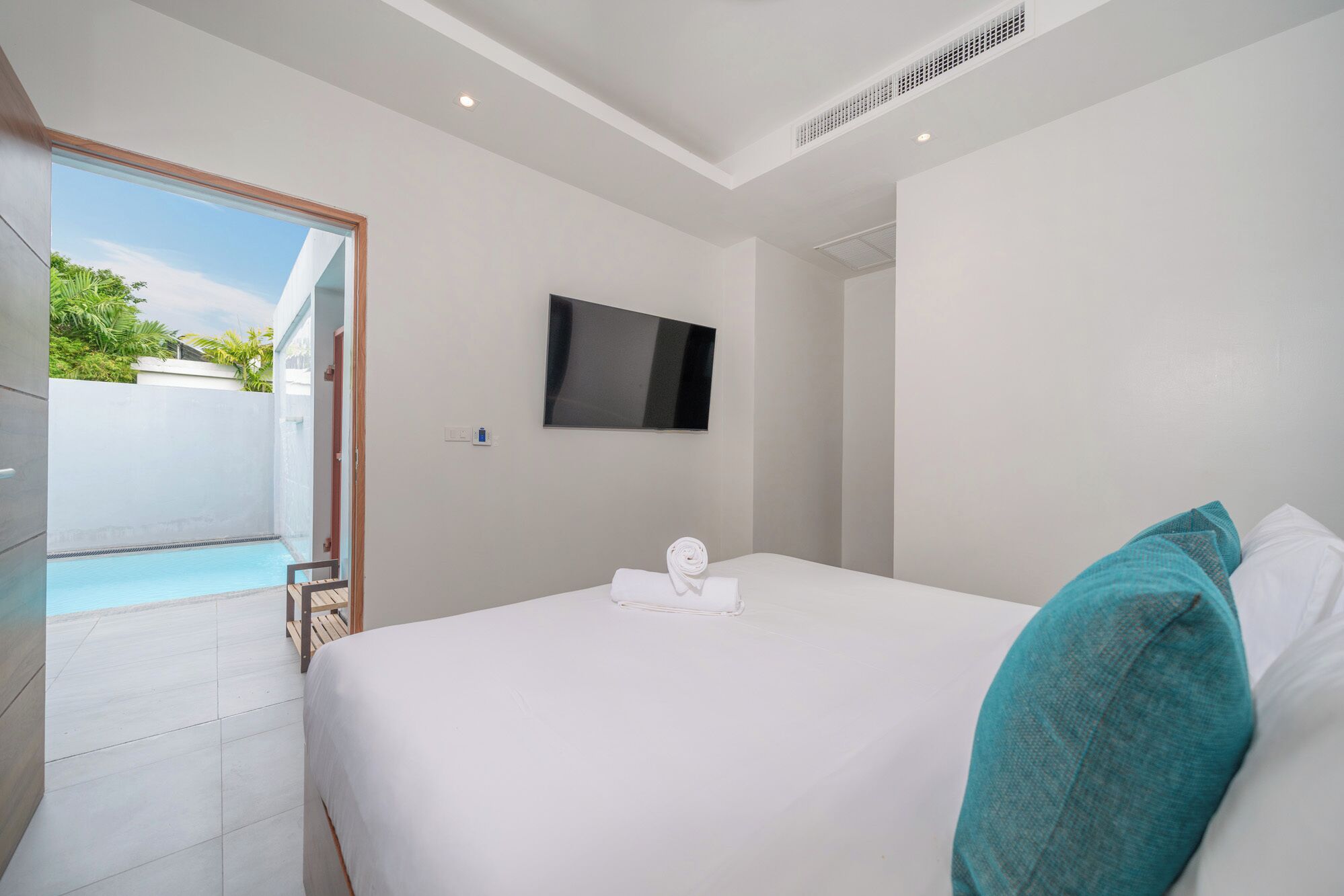 A hotel room with a bed, a TV mounted on the wall, and a view of a swimming pool.