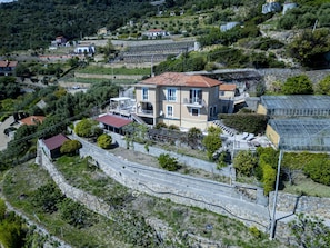 A hillside residential area with a two-story house featuring a red-tiled roof, a balcony, and a small attached structure with a red roof. - Spacious villa with sea views (Cipressa)