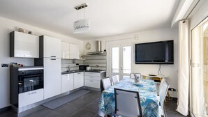 Una cocina moderna con armarios blancos, horno empotrado y comedor con mesa para dos.