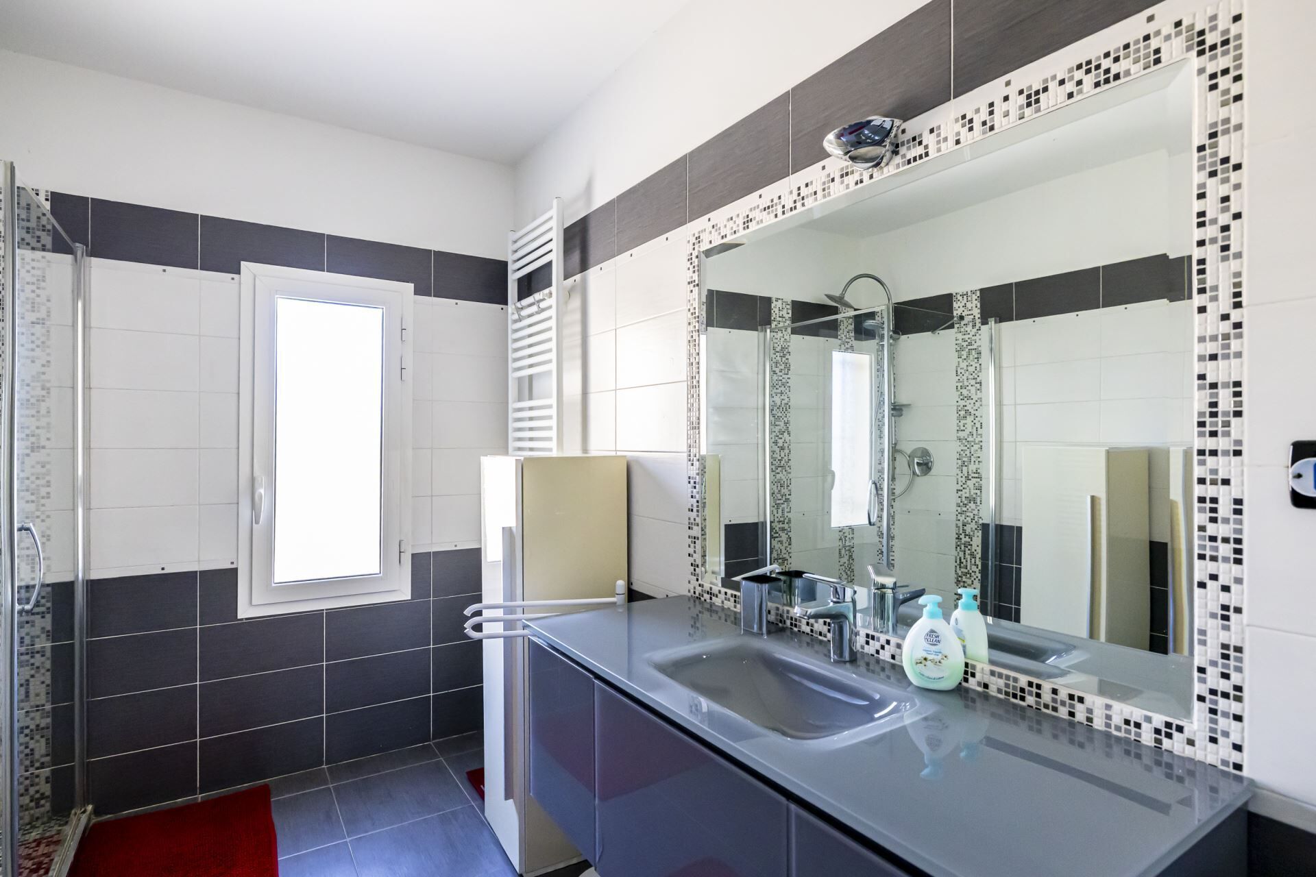 Une salle de bain moderne avec un grand miroir, un lavabo et un espace douche.