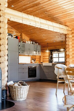 A log cabin interior with a kitchen, dining area, and a fireplace. - Authentic log house amid evergreens in Vendsyssel (Fjerritslev)