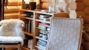 Een gezellig chaletinterieur met een houten wand, een geweven stoel, een boekenkast en een open haard.