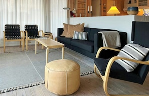 Ein Wohnzimmer mit einer Couch, zwei Sesseln, einem Couchtisch und einem runden Hocker.