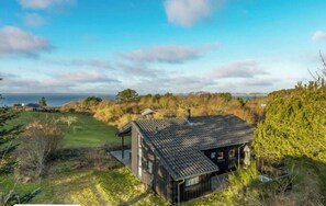 Eine rustikale Holzhütte mit geneigtem Dach, umgeben von einer grünen Landschaft und dichtem Grün.