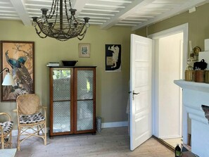 Een kamer met een houten kast, een rieten stoel, een kroonluchter en een witte deur.