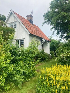 Een wit gebouw met een rood dak, omringd door groen en gele bloemen.