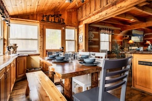 A wooden cabin interior with a dining table set for four, wooden walls, and a kitchen area with a sign reading "WELCOME TO". - Rustic Cove - Hot Tub, Game Room, Dog Friendly (Pigeon Forge)