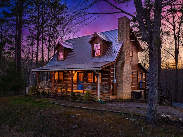 A log cabin with a metal roof, a stone chimney, and a porch with a railing. - Rustic Cove - Hot Tub, Game Room, Dog Friendly (Pigeon Forge)