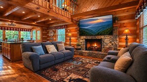 Ein Holzblockhaus-Innenraum mit Kamin, großem Fernseher und gemütlichem Sitzbereich.