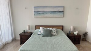 A bed with a textured light green bedspread, two nightstands with lamps, a framed picture, and a potted plant. - Luxury Beachfront Beauty (San Bruno)