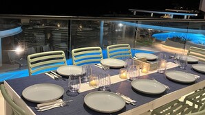 An outdoor dining area with a glass table, chairs, and a pool in the background. - Luxury Beachfront Beauty (San Bruno)