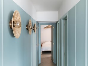 Un pasillo con paredes azul claro, una cama a lo lejos y lámparas fijadas a la pared.