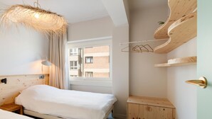 Ein Schlafzimmer mit einem Bett, einem Nachttisch, einer Hängeleuchte und einem Fenster mit Blick auf Gebäude.