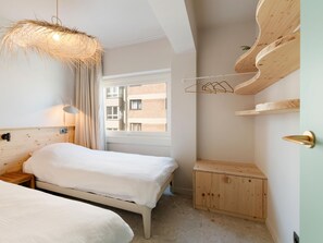 Ett sovrum med en säng, ett nattduksbord, en hängande lampa och ett fönster med utsikt över byggnader.