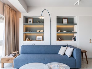 Una sala de estar moderna con un sofá azul, una mesa de centro y estanterías empotradas con objetos decorativos.