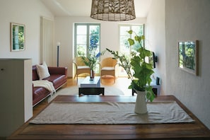 Ein Wohnzimmer mit Sofa, Sesseln, Couchtisch, Teppich, Pflanze und einem Esstisch.