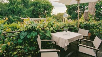 Un patio al aire libre con una mesa y sillas, rodeado de follaje y un árbol.