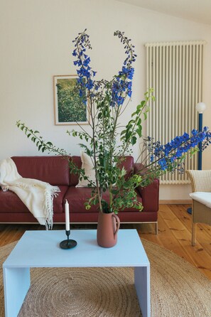 Ein Wohnzimmer mit einem weißen Couchtisch, einem roten Sofa, einer Topfpflanze und einem Bild an der Wand.
