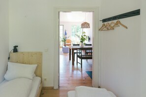 Ein Schlafzimmer mit Holz-Kopfteil, einem Bett mit weißer Bettwäsche, Holzboden und einer Tür zu einem Essbereich mit Tisch und Stühlen.