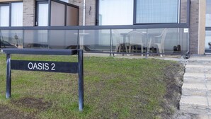 Een modern gebouw met een bordje waarop 'OASIS 2' staat, grote ramen en een gazon met buitenmeubilair.