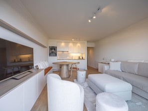 Ein modernes Wohnzimmer mit Sofa, Hocker und einem Essbereich mit Tisch und Stühlen.