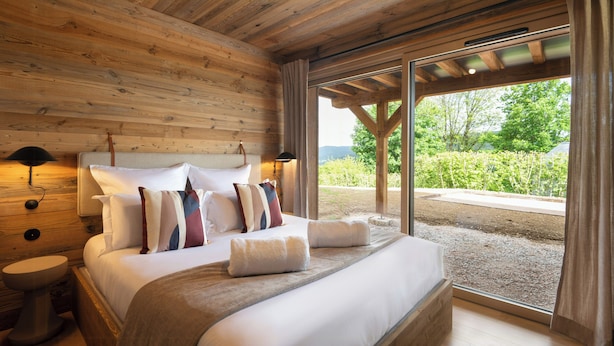 Un dormitorio con paneles de madera, una cama grande, dos lámparas de noche y vistas a la vegetación exterior.