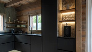 Una cocina moderna con armarios negros, una cafetera y una botella de vino en un estante.