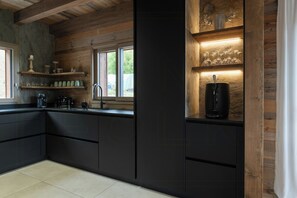 A modern kitchen with black cabinetry, a coffee machine, and a wine bottle on a shelf. - Family chalet with Vosges mountain views in Gérardmer (Gérardmer)