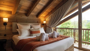 Un dormitorio de cabaña de madera con una cama grande, cabecera, lámparas de noche y un balcón con vistas.