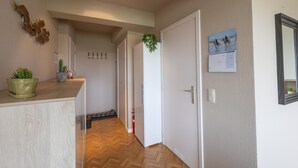 Un couloir avec un plancher en bois, un porte-manteau, une porte et un calendrier accroché au mur.