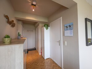 A hallway with a wooden floor, a coat rack, a door, and a calendar on the wall. - Modern apartment with sea view and sunny terrace (Middelkerke)