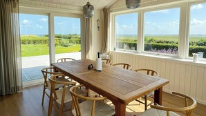 Ein Essbereich mit Holztisch und Stühlen, großen Fenstern mit Blick auf Grünflächen und einer strukturierten Decke.