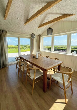 A dining area with a wooden table and chairs, large windows with a view of greenery, and a textured ceiling. - Summer house with wilderness bath and water views (Vinderup)