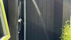 Eine Holzterrasse führt zu einer dunklen Duschkabine aus Holz mit einer Metallrohrleitung.