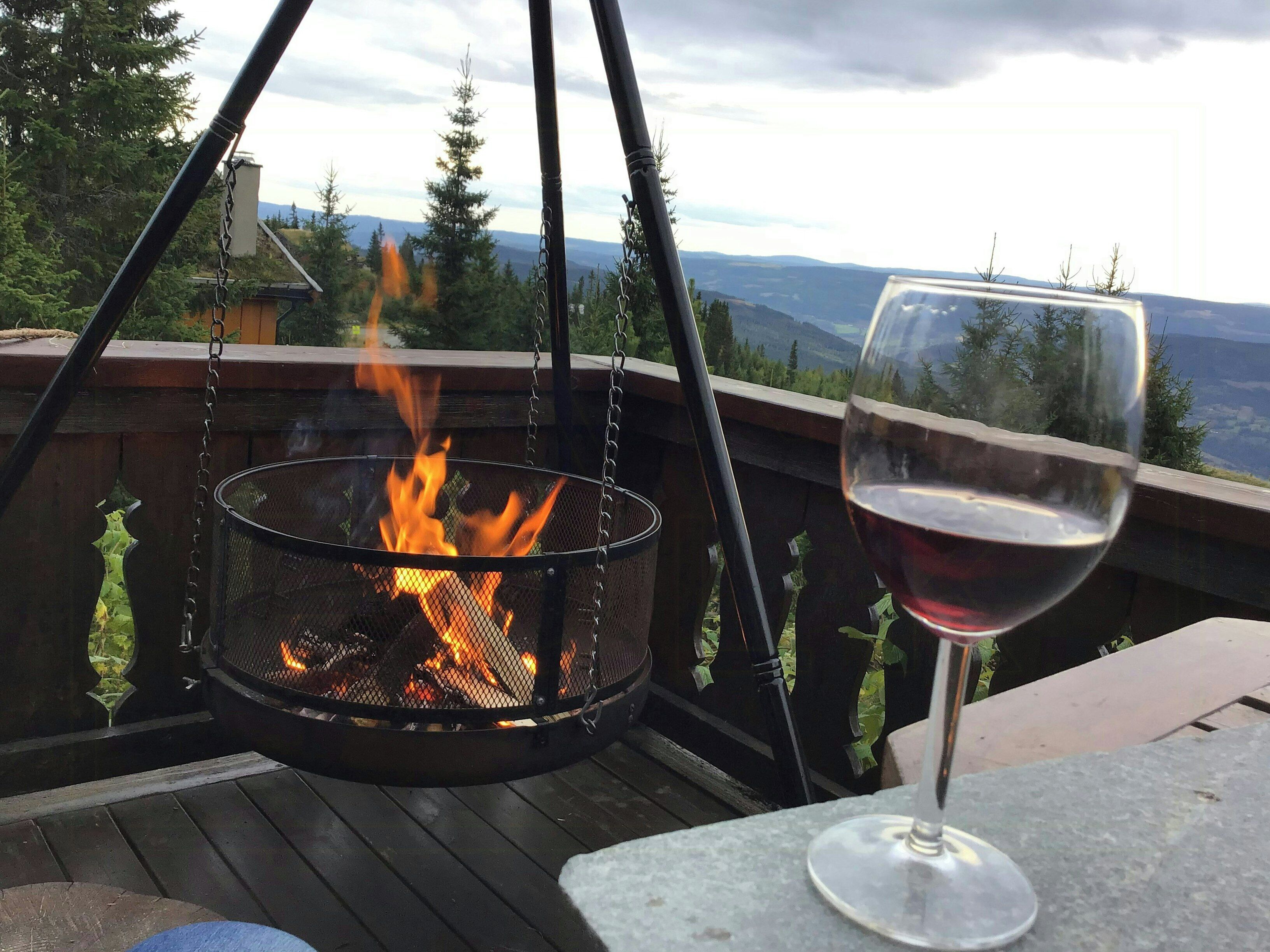 Bålsted med flammer, et glas rødvin og udsigt til bjerge.
