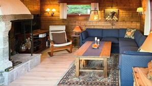 A cozy cabin interior with a stone fireplace, wooden walls, a blue sofa, and a dining table. - Spacious family cabin with views in Hafjell (Øyer)