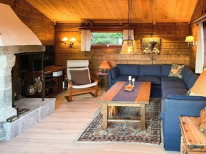 Ein gemütliches Blockhaus-Interieur mit Kamin aus Stein, Holzwänden, einem blauen Sofa und einem Esstisch.