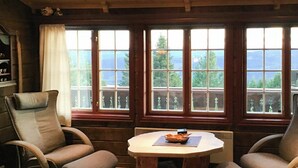 A cozy room with a wooden table, two chairs, and large windows offering a view of trees and mountains. - Spacious family cabin with views in Hafjell (Øyer)