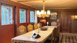 A dining room with a long table, chairs, a chandelier, and a fireplace. - Spacious family cabin with views in Hafjell (Øyer)