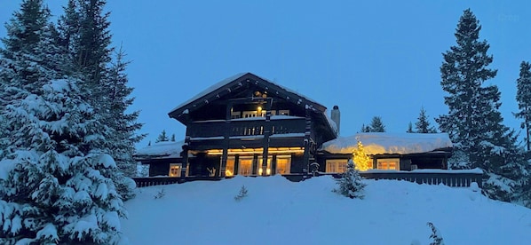Ein großes Blockhaus mit mehreren Ebenen, umgeben von schneebedeckten Bäumen.