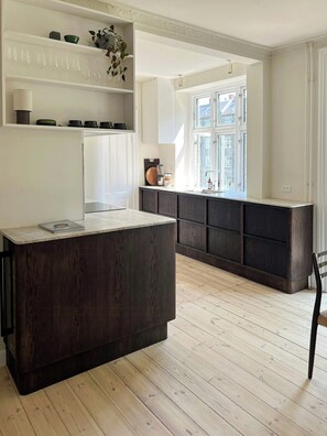 A modern kitchen with a central island, dark wood cabinets, and a window providing natural light. - Classic flat near Frederiksberg Gardens (København)