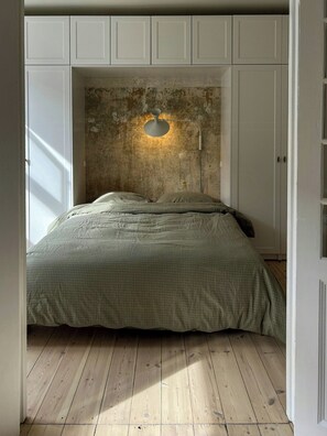 A bedroom with a bed, wooden flooring, and a wall with a circular window. - Classic flat near Frederiksberg Gardens (København)
