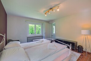 Un dormitorio con dos camas, una ventana, un radiador, una mesita de noche, una lámpara y un espejo.